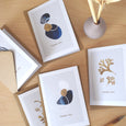 A beautiful set of 5 Thank You note cards, complete with kraft envelopes. Card designs feature blue and gold beach inspired illustrations, including seaweed and pebbles.